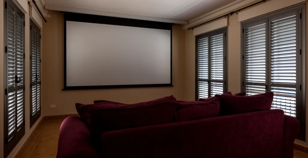 Sala de cine en casa con contraventanas cerradas filtrando luz exterior para mejor aislamiento acústico